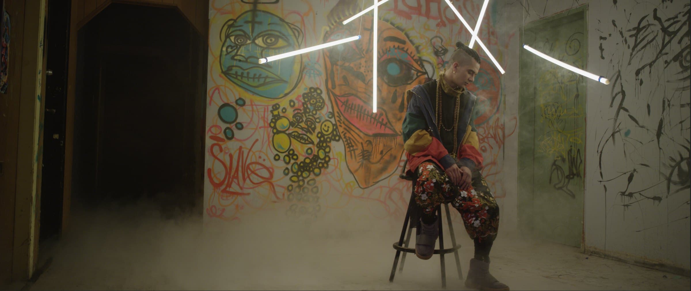 Bdice seated in a graffiti room under light bars